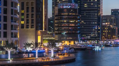 Dubai Marina rıhtımı kuleleri, rıhtımda restoranları ve Dubai 'deki köprüden geceye geçiş zamanı, Birleşik Arap Emirlikleri. Gün batımından sonra yapay kanallı bölge