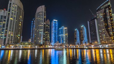 Dubai Marina gezinti güvertesinde yatlar ve modern kuleler Dubai 'deki deniz kıyısından yansıyan su, Birleşik Arap Emirlikleri' nin gece hiperhızlandırması. Yapay kanalla aydınlatılmış bölge