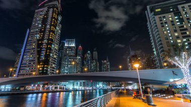 Köprü manzaralı Dubai Marina 'nın güvertesinde yürümek, deniz kenarındaki Birleşik Arap Emirlikleri gecesinden suya yansıyan modern kuleler. Çevresinde yapay kanallar ve aydınlık gökdelenler olan bir bölge.