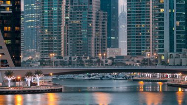 Dubai Marina Kanalı, modern kuleleri ve yatları olan liman kenti Dubai 'deki köprüden gece gündüz geçiş zamanı olan Birleşik Arap Emirlikleri' ne yansıyor. Güneş doğmadan önce etraftaki gökdelenler
