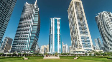 Rıhtımdaki palmiyeli gökdelenlerin hızlandırılmış görüntüsü. Dubai, BAE 'deki parkın yakınındaki Jumeirah Gölü Kuleleri' nde camla kaplı konut binaları. Parktan görüntüle