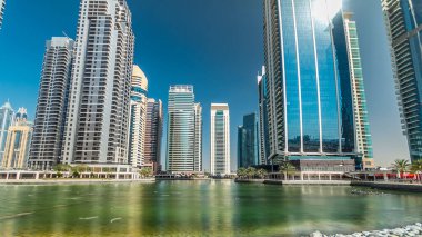 Rıhtımdaki palmiyeli gökdelenlerin hızlandırılmış görüntüsü. Jumeirah Gölü Kuleleri 'nde camla kaplı yerleşim yerleri Dubai, BAE' deki suya yansıdı. Rıhtımdan görüntüle