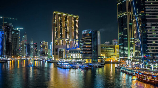 Dubai Marina promenade with yachts and modern towers with restaurants from bridge night timelapse hyperlapse, United Arab Emirates. Cafes and restaurants