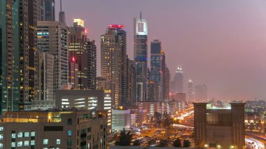 Dubai Kuleleri 'nin şehir merkezinden gece gündüz geçiş zamanı. Gün batımından sonra Şeyh Zayed 'in gökdelenli hava manzarası. Yolda ve otoparkta trafik vardı.