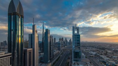 Dubai gökdelenleri akşam saatlerinde güneş camlarında yansıyor. Dubai metro istasyonu ve Şeyh Zayed Yolu 'ndaki trafik. Kule çatısından gökyüzü görüntüsü. Renkli bulutlu gökyüzü ve güneş ışığı