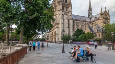 Notre-Dame de Paris zaman atlaması. Fransa, Paris 'teki Cite Adası' ndaki ortaçağ Katolik katedrali. Gün batımından önce Çifte Köprü 'den görüntü. Yürüyen turistler. Yaz gününde bulutlu bir gökyüzü