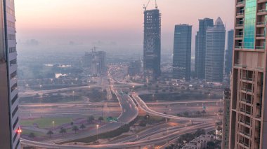 Havadan görünümü bir yol kavşak ve bir büyük şehir gece gün geçiş timelapse için modern kuleleri. Arabalar ve gökdelenler ile UAE Dubai Yat Limanı bölgesinin kentsel peyzaj.