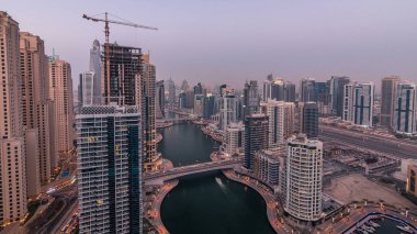 Günden geceye güzel bir hava manzarası. Dubai, BAE 'de gün batımından sonra yüzen yatları ve tekneleri olan Dubai Marina gezinti ve kanallarının panoraması. Modern kuleler ve yoldaki trafik.