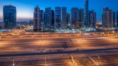 Jumeirah lakes hava görünümünü gün geçiş timelapse Şeyh zayed road ve metro hattı üzerinde trafik ile gecesine ışıklandırılmış gökdelenler ile kuleleri. Dubai Yat Limanı güneş doğmadan önce çatı görünümü