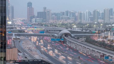 Jumeirah göl kulelerinin, gökdelenlerin ve Al Barsha bölgesinin gece gündüz geçiş zamanının havadan görüntüsü. Golf sahası ve metro hattı yakınlarındaki Şeyh Zized yolunda trafik var..