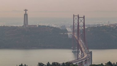 Lisbon and Almada during sunrise with traffic on April 25 bridge from a viewpoint in Monsanto at morning timelapse. Aerial top view with Cristo Rei monument. Foggy weather