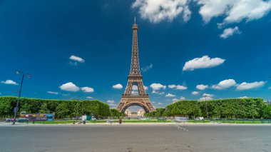 Paris 'teki Champs de Mars' taki Eyfel Kulesi. Zaman atlaması, Fransa. Yazın mavi bulutlu gökyüzü, yeşil çimenler ve etrafta trafik olan çeşme.