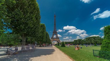Paris 'teki Champs de Mars' taki Eyfel Kulesi. Zaman atlaması, Fransa. Yazın mavi bulutlu gökyüzü Ağaçlı yeşil çimenler ve etrafta yürüyen insanlar.