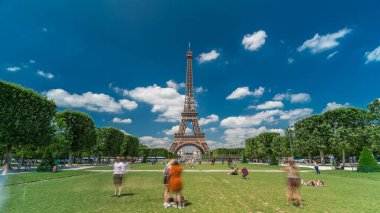 Paris 'teki Champs de Mars' taki Eyfel Kulesi. Zaman atlaması, Fransa. Yazın mavi bulutlu gökyüzü yeşil çimlerle kaplı ve insanlar etrafta dolaşıyor. İlerliyorum.
