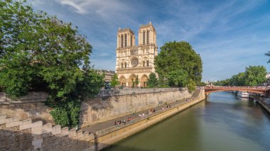 Notre Dame de Paris katedralinin ön cephesinde, nehir ve kıyı şeridi hiperhızlandırılmış. Köprüden panoramik görüntü. Yazın mavi bulutlu gökyüzü