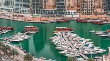 Dubai Marina körfezindeki iskeleye park etmiş lüks yatlar. Şehir hava manzaralı zaman ayarlı. Sabah erken saatlerde kuleler ve gökdelenler