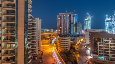Dubai Marina 'da aydınlık gökdelenler ve gece gündüz gezinti güvertesi geçiş zamanı. Yol trafiği olan modern kuleler ve tekneler. Birleşik Arap Emirlikleri