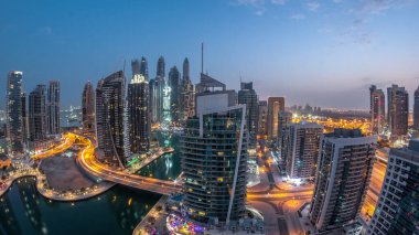 Dubai Marina konutları ve ofis gökdelenlerinin panoramik hava manzarası. Gün doğumundan önce gece gündüz geçiş zamanı. Yüzen tekneler ve yatlar. Yolda trafik vardı.