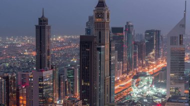 Sheikh Zayed Yolu yakınlarındaki binaların silueti ve Dubai, BAE 'deki hava trafiği gece gündüz değişiyor. Gündoğumundan önce finans merkezinde ve şehir merkezinde modern kuleler ve aydınlık gökdelenler