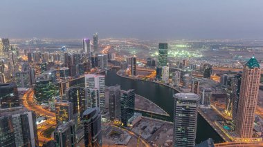 Dubai'deki iş bölümü kulelerinin panoramik havadan görünümü gece geçiş saati. Gün batımından sonra yapım aşamasında olan bazı gökdelenler, kanal ve yeni kulelerin çatı görünümü.