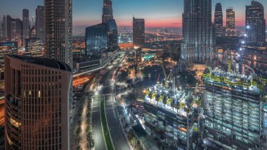 Gün doğmadan Dubai şehir merkezindeki panoramik gökyüzü manzarası alışveriş merkezi, çeşme ve trafik ile gece gündüz geçiş zamanı. Modern gökdelenler ve inşaat alanı