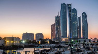 Al Bateen marinası Abu Dabi. Gün batımından sonra tekneler ve arka planda aydınlatmalı modern gökdelenler.