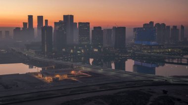 Abu Dabi şehrinin gökdelenleri aydınlanmadan önceki gökdelenleri gece gündüz geçiş zamanı. Çatıdan sisli bir sabahta köprüden hava manzarası ve yol trafiği