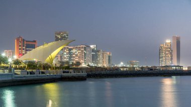Abu Dabi 'deki gezinti alanı gün batımında aydınlandı, gece gündüz geçiş zamanı, Birleşik Arap Emirlikleri. Arka plandaki gökdelenler suya yansıdı