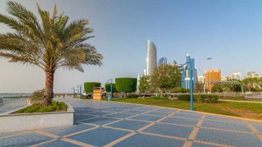 Abu Dabi 'nin sahil şeridi boyunca uzanan Corniche Bulvarı plajı parkında arka planda gökdelenler var. Avuçlar yana. Güneşli bir günde mavi gökyüzü