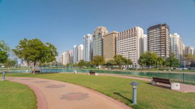 Abu Dabi 'nin sahil şeridi boyunca uzanan Corniche Bulvarı plajı parkında arka planda gökdelenler var. Lake Park 'ın manzarası. Bir tarafta ağaçlar. Güneşli bir günde mavi gökyüzü