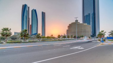 Abu Dabi 'nin gökdelenleri gün batımında Etihad Kuleleri' nin zaman ayarlı binalarıyla aydınlandı. Avuç içleriyle ve trafiğiyle park et. Birleşik Arap Emirlikleri