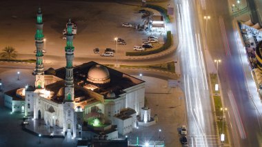 Camii olan Ajman 'ın şehir manzarası ve çatıdan yola çıkan trafik gece vakti aydınlatılmış binaların ışıkları. Birleşik Arap Emirlikleri.