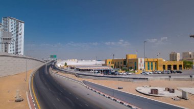 Ajman 'da üst geçitte yol trafiği, köprüden gündüz vakti havadan görüntü. Birleşik Arap Emirlikleri 'nin arka planında kuleleri olan şehir manzarası.