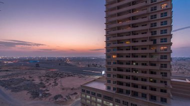 Ajman 'da çatıdan gece kuleye kule ve kavşakta trafik olan şehir manzarası. Birleşik Arap Emirlikleri 'nde gün batımından sonra aydınlanan binaların hava manzarası.