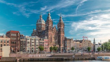 Merkez İstasyonu yakınlarındaki Amsterdam 'daki Eski Merkez' de Aziz Niklas Bazilikası 'nın hiperlapası. Tekne istasyonunun oradaki limanda yürüyen insanlar. Amsterdam, Hollanda