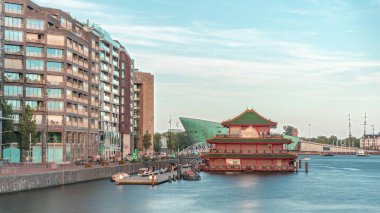 Sudaki pagoda şeklinde bir Çin restoranının hipervanesi, tarihi şehir merkezi binalarının ve günbatımında modern mimarinin arka planına karşı kurulur. Amsterdam, Hollanda
