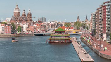 Amsterdam 'ın Merkez İstasyonu yakınlarındaki Eski Merkezi' nde Aziz Nicholas Bazilikası 'nın bulunduğu havacılık manzarası. İnsanlar rıhtım boyunca tekne istasyonuyla yürüyorlar. Amsterdam, Hollanda