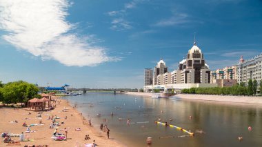 İnsanlar, Astana, Kazakistan 'daki köprüden ve ufuk çizgisinden gelen yapay bir plaj zaman atlaması boyunca bir nehirde banyo yapıyorlar. Nur-Sultan şehri