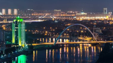 Nehir ve aydınlık köprü Astana 'da gece vakti çatıdan su havası saatine yansıyor. Nur-Sultan şehri, Kazakistan başkenti