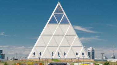 Barış ve Uzlaşma Sarayı 'nın dışında park ve fıskiyelerle birlikte zaman ayarlı bir bina var. Nur-Sultan şehri, Kazakistan.