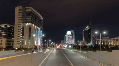 Kunaev Bulvarı 'ndaki gece trafiği aşırı hızlandı. Modern bina geceleri arka planda aydınlanıyor. Nur-Sultan şehri, Kazakistan.