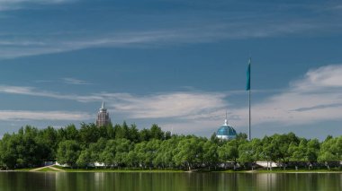 Ishim nehrinin rıhtımı. Bayrak, bina, yürüyüş yolu ve ağaçlarla dolu. Güneşli bir gün. Nur-Sultan şehri, Kazakistan