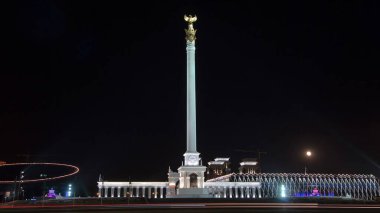 Stele anıtı Kazak Eli ve kuş Samruk geceleri ve Bağımsızlık Sarayı hiperhız ve trafik ön planda. Nur-Sultan şehri, Kazakistan