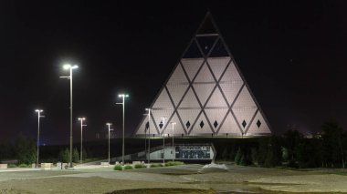 Gece, Barış ve Uzlaşma Sarayı 'nın yanında renkli fıskiyelerle dolu bir meydan. Kazakistan' ın Nur-Sultan şehrinde zaman kavramını aydınlatan bir bina.