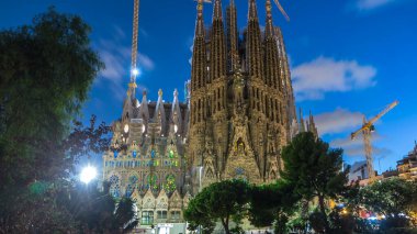 Sagrada Familia: İspanya 'nın Barcelona kentindeki Iconic Roma Katolik Kilisesi' nin Gündüzden Geceye Geçiş Süreci. Kuleler ve Turnalar Yakınlardaki Gölün Huzurlu Sularında Yansımaya Karşı Duruyor