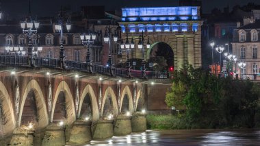 Geceleyin Porte de Bourgogne, Fransa 'nın Bordeaux kentindeki Garonne Nehri' nin üzerindeki süslenmiş sokak lambalarıyla aydınlatılmış Pont de Pierre taş köprüsü. Yansımaların ve şehir ışıklarının çarpıcı zamanlaması