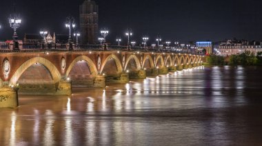 Fransa 'nın Bordeaux kentindeki Porte de Bourgogne' un aydınlatıldığı, gece Garonne Nehri üzerinde süslenmiş sokak lambaları olan Pont de Pierre Stone Köprüsü. Yansımaların ve şehir ışıklarının çarpıcı zamanlaması