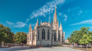 Saint-Andre de Bordeaux Katedrali. Mavi gökyüzünün altında ikiz kuleleri olan hızlandırılmış zaman atlaması. Yeşil ağaçlar ve meydanda yürüyen insanlar sakin bir şehir atmosferi yaratıyor. Bordeaux, Fransa