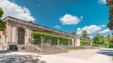 Fransa 'nın başkenti Jardin' de Palais du Capitole 'de zaman atlaması. Sarmaşık kaplı yeşil ağaçlar, merdivenler ve parlak mavi bulutlu gökyüzü ile çevrili tarihi bir binanın manzarası.