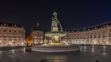 Panorama, Place de la Bourse 'u ve Fransa' nın Bordeaux şehrindeki çeşmeleri gösteriyor. Aydınlatılmış tarihi binalar büyük meydanın sınırında. Trafik ve sokakta hareket sahneyi güçlendirir